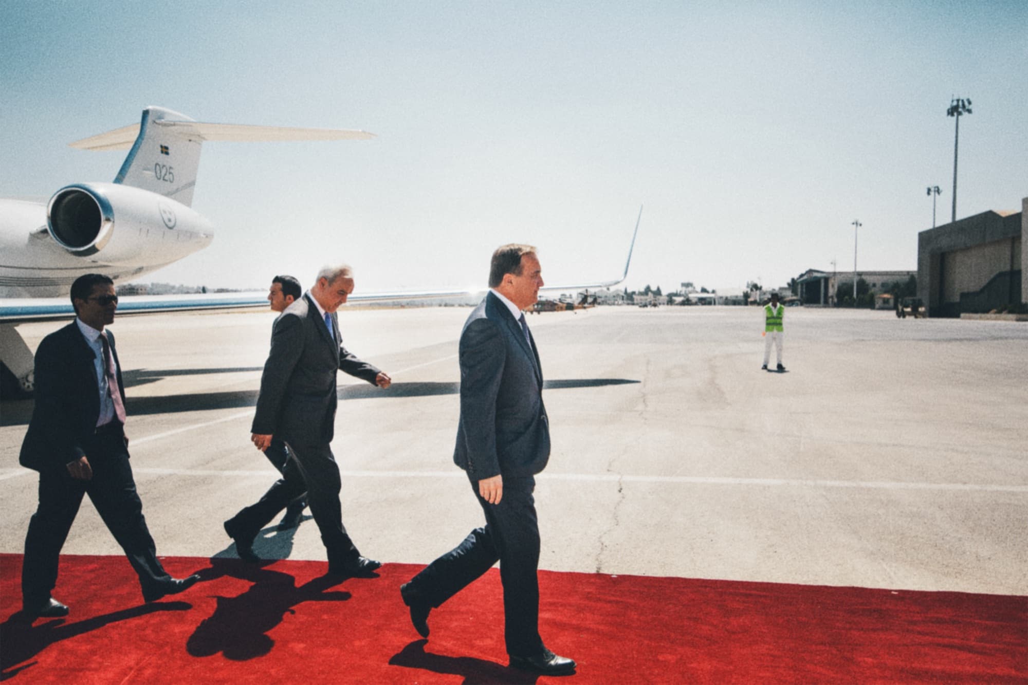 A delegation walking along a red carpet beside an aircraft