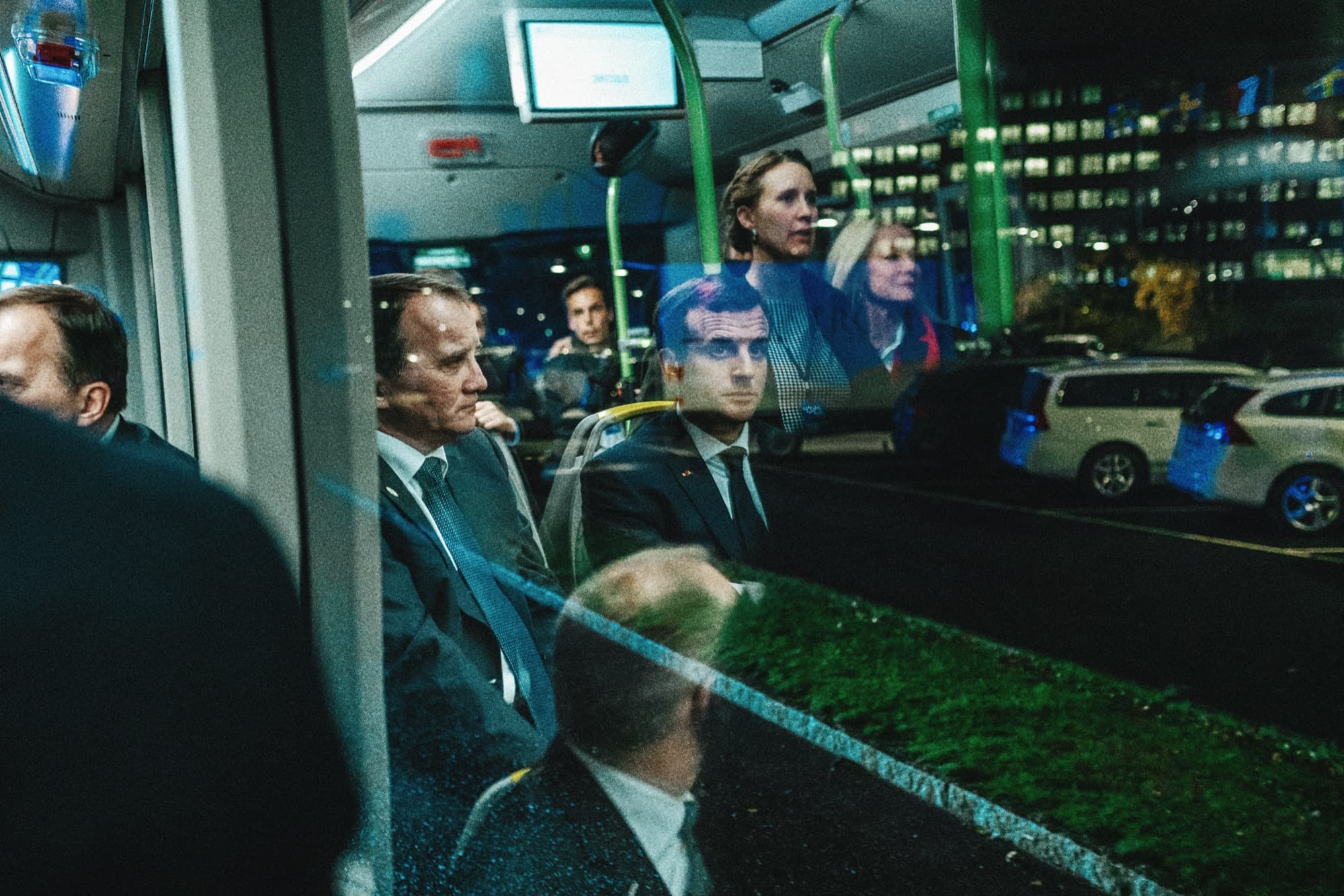 A delegation travelling on a bus, reflected in the window against city lights
