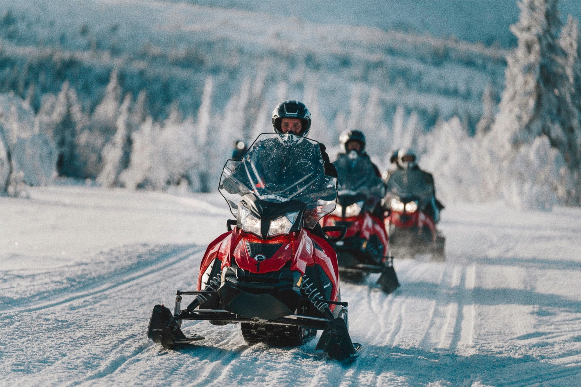 A group riding snowmobiles through a snowy landscape